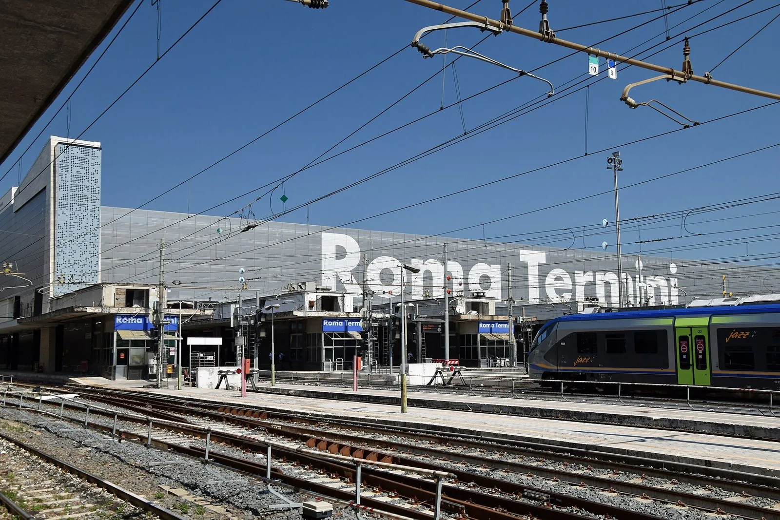 I binari della stazione Roma Termini con la grande scritta sulla facciata e un treno regionale in sosta