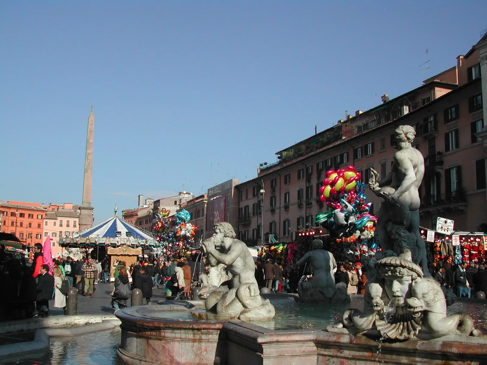 Piazza Navona durante le feste natalizie, con bancarelle, palloncini, una giostra e la Fontana del Moro in primo piano